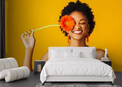 Portrait of a happy young woman holding orange Gerbera daisy covering her eye with eyes closed Wall mural