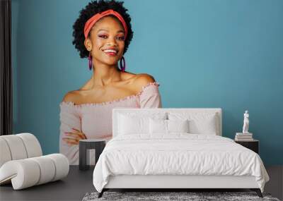 Portrait of a happy young woman with loop earrings smiling and looking at camera arms crossed, isolated on blue color background Wall mural