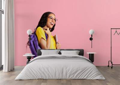 Portrait of a  laughing  young female student with book, backpack and glasses ready for school looking at  pink studio copy space Wall mural