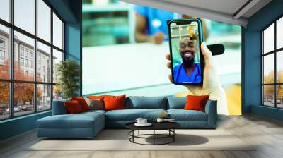 Portrait of a sick patient coughing into tissue being helped via tele medicine by a male doctor wearing blue scrubs uniform using smartphone mobile phone Wall mural