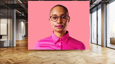 Portrait of a smart young woman in pink shirt and glasses, isolated on pink studio background Wall mural