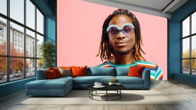 Portrait of a smiling young man in striped shirt with 'happy' sign and big sunglasses, standing in front of a pink background.. Wall mural