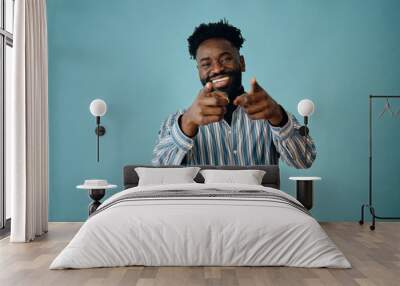 portrait of a young african american man with a beard smiling and pointing at camera and a blue shirt on a gray background Wall mural