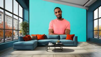 Portrait of a young man smiling with arms crossed, against blue studio background Wall mural