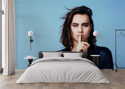 Portrait of a young man with long hair and finger on mouth in studio Wall mural