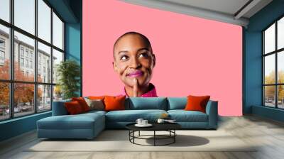 portrait of a young woman in pink shirt with finger on mouth looking up thinking, isolated on pink s Wall mural