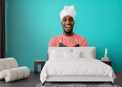 Portrait of an excited young male chef with arms crossed and mouth open, against blue studio background Wall mural