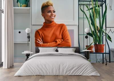 Portrait of happy young woman with arms crossed standing  at home looking out the window Wall mural