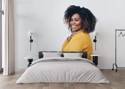 Profile of African American mid aged woman with curly hair and one hand on her shoulder looking at camera and smiling.  Wall mural