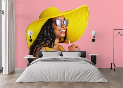 Profile portrait of a young smiling woman with yellow summer hat and sunglasses holding a drinking cup and paper straw Wall mural