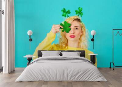 Studio portrait of a smiling young woman holding shamrock covering one eye, with St. Patrick's Day head decoration Wall mural