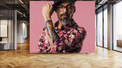 Vertical portrait of a very cool man with tattoos, tilting his hat, isolated on pink studio background Wall mural