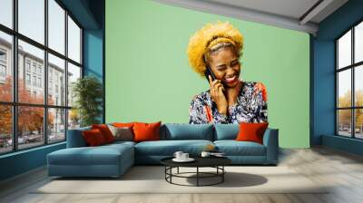 Young woman smiling while talking the phone, isolated on green studio background Wall mural