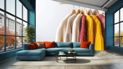 A rack of clothes with a white sweater hanging on the left, a yellow sweater hanging in the middle, a red sweater hanging on the right, and a pink sweater hanging in the middle Wall mural