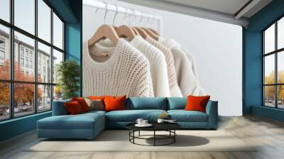 A rack of white and tan sweaters hanging on a white wall. The sweaters are all different colors and styles, but they all have a similar texture and feel. Scene is cozy and comfortable Wall mural