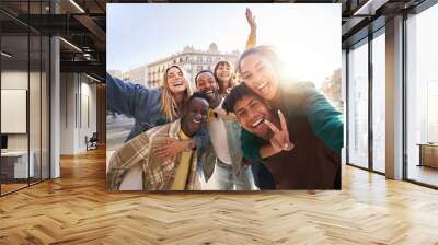 A group of cheerful students college friends having fun together as they travel through European cities. Happy community of diverse people. Selective focus on the smily couple taking the selfie. Wall mural