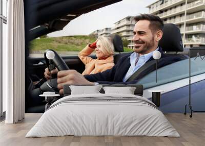 A happy middle-aged couple travel by car to go to their date. The wife enjoys the ride while the husband drives with a smile. Concept of relationship, weekend and leisure. Wall mural