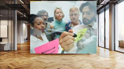 Creative colleagues meeting in office. Diverse business people team workers standing in brainstorming, discussing new ideas for the future of the company, writing on paper note.  Wall mural