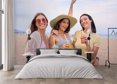 Excited group generation z European women together posing on beach embracing looking smiling at camera. Cheerful girls friends holding fruit smoothies enjoying their summer holidays in Mediterranean Wall mural