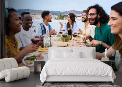 Gathering of happy people around meal table with wine glasses and food celebration terrace barbecue party. Young multiracial friends enjoying laughing together lunch time on summer weekend on rooftop Wall mural