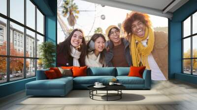 Group four cheerful multiracial young friends posing portrait in winter clothes. Happy people looking at camera smiling amused outdoor. Colleagues gathered at amusement park. College on field trip. Wall mural