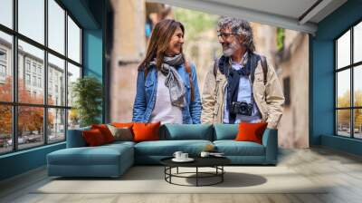 Happy mature romantic couple look at each other smiling on tourist street. Pensioners enjoying leisure time together on holidays. Middle-aged husband and wife in love holding hands outdoor Wall mural