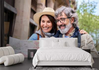 Mature couple in their sixties smiling looking at map in European city street. Happy seniors enjoying vacation or weekend getaway together. Concept of travel, leisure and lifestyle in retirement.  Wall mural