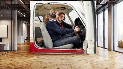 Pilot in training and flight instructor in the cockpit of an airplane. Female pilot with headphones preparing to fly. He is sitting next to the female instructor attending to her explanations. Wall mural