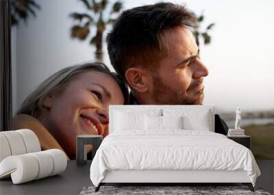 Portrait happy and relaxed couple on vacation or weekend getaway. Laughing wife leaning on husband shoulder. Loving partners enjoying a romantic trip. People looking at the horizon. Wall mural