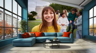 Portrait of a Young red-haired girl with wide smile and piercing look at the camera. Group of friends gathered in the background of the image. Colleagues hanging out in the city. Outdoors. Wall mural