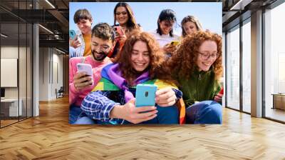 Smiling young friends using mobile phone celebrating gay pride festival day together. Happy LGBT people community with rainbows flags watching and checking social networks outdoor Wall mural