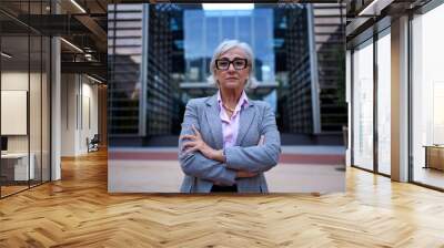 Successful and serious middle-aged business gray woman with arms crossed at workplace looking at camera. Mature female entrepreneur outside the office with proud attitude and empowered. Copy space  Wall mural