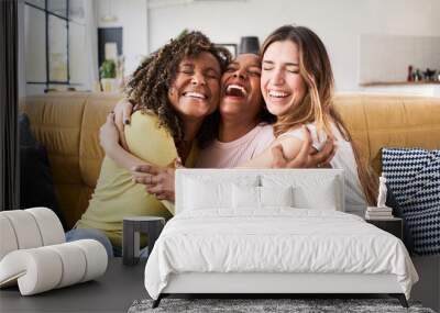 Three happy friends hugging smiling.Funny women together celebrating sitting on the living room sofa Wall mural