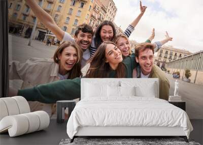 Tourist group of young excited friends together posing happy for photo in city square. Gen z people smiling with arms raised in air for holiday souvenir picture enjoying having fun in European town Wall mural