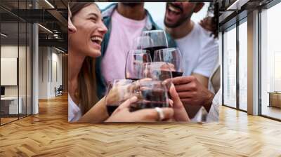 Vertical group multiracial excited friends toasting red wine and celebrating party outdoors. Young people together cheers on open air. Boys and girls enjoying free time on summer weekend vacation. Wall mural