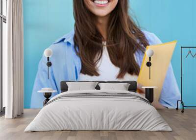 Vertical portrait on blue background of smiling and cheerful young Caucasian girl. Pretty student woman holding yellow folder. Happy college people posing and looking at camera. Copy space. Wall mural