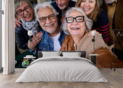 Vertical. Happy mature gray hair woman taking selfie of group seniors Caucasian cheerful friends posing together sitting at cafeteria. Older people looking laughing at camera with snacks on table Wall mural