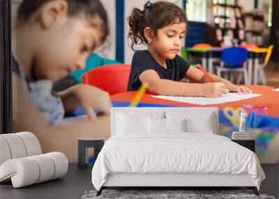 Two Latina girls coloring in a kindergarten classroom, surrounded by scissors, educational games, and coloring supplies Wall mural