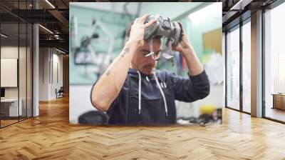 Portrait of an hispanic young worker removing a respiratory protection mask, as he finishes a spray painting job in his workshop. Health protection in industrial work. Real people working. Wall mural