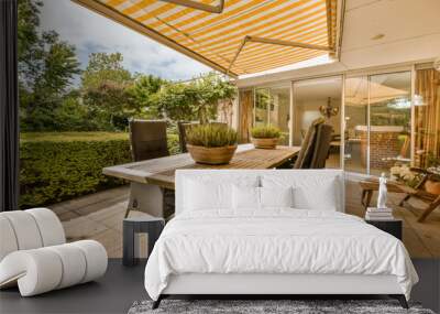 an outdoor dining area with table and chairs under the awning on a sunny day in the patio is surrounded by lush green trees Wall mural