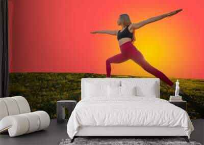 Woman Doing Yoga on Grass in Warrior 2 Pose With Copy Space Orange Background Wall mural