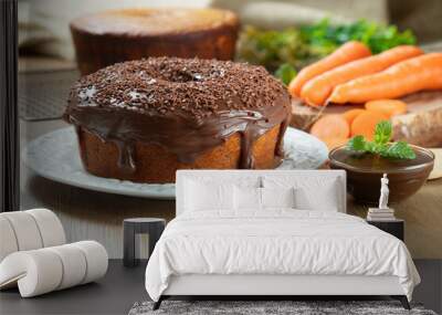 Brazilian carrot cake with chocolate frosting on wooden table with carrots in the background Wall mural