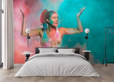 Carefree cheerful woman covered in rainbow colored powder celebrating the festival of colors. Young woman having fun with colorful holi powder Wall mural