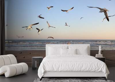 Two girls feeding flying seagulls on the beach Wall mural