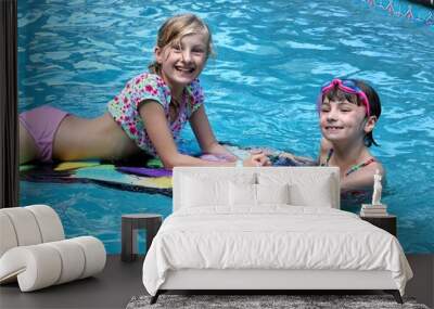 Two girls having fun in the pool with a kickboard smiling at the camera Wall mural