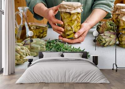 Artichoke hearts marinated with olive oil and herbs. Woman holding a glass jar with pickled artichokes. Homemade healthy eating. Wall mural