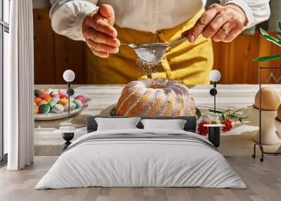 Female hands sprinkles Easter cake with icing sugar through sieve. Anonymous woman making traditional easter cake or sweet bread with topping. Easter treat. Wall mural