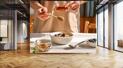 Woman preparing healthy dieting vegan nutritious breakfast. Female hand pouring honey in the bowl with oatmeal porridge with walnuts and blueberries. Wall mural