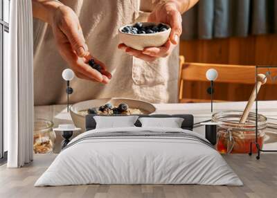 Woman preparing healthy dieting vegan nutritious breakfast. Female hand putting blueberries in the bowl with oatmeal porridge with walnuts and honey. Wall mural