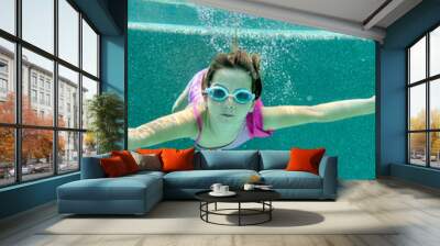 Girl swimming underwater in a pool wearing goggles and a pink swimsuit Wall mural